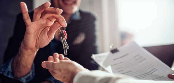Handoff of a set of keys between two people, one person is holding lease documents. 